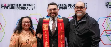 A student with a cultural stole posing with parental figures.